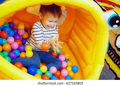 Boy Playing With Colored Balls In The Bouncy House At The Playground In The Room. Colorful Plastic Balls, The Joy On A Child's Face, A Playful And Funny Guy.