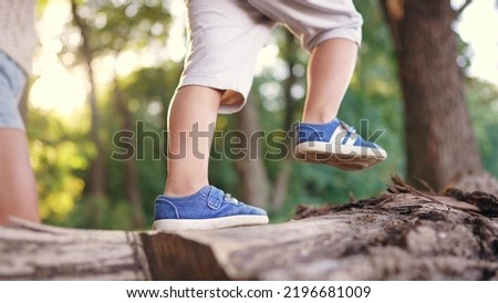 the boy is playing in the forest park. close-up child legs walking on a log of a fallen tree. happy family childhood dream concept. a child in sneakers walks on fallen lifestyle tree in park
