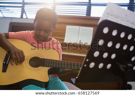Boy playing guitar while sitting in classroom at school