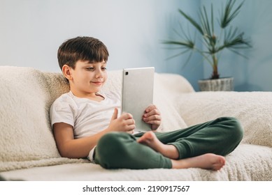 Boy Playing Mobile Game On Tablet On Sofa. Preschooler Playing Mobile Games. Kid Using Device For Gaming. Child Playing Video Game At Home. Communication And Chat Device