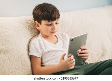 Boy Playing Mobile Game On Tablet On Sofa. Preschooler Playing Mobile Games. Kid Using Device For Gaming. Child Playing Video Game At Home. Communication And Chat Device