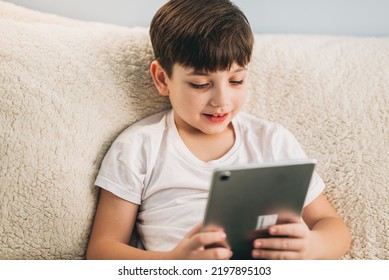 Boy Playing Mobile Game On Tablet On Sofa. Preschooler Playing Mobile Games. Kid Using Device For Gaming. Child Playing Video Game At Home. Communication And Chat Device