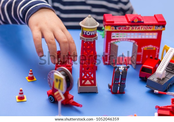 boy playing\
with a set of plastic toys at a fire station. child playing with\
toys on a plastic blue table at\
home.