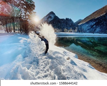 A boy is playing with snow in Alps in a sunny winter day near the beautiful alpine lake. Quality family time, enjoining winter. Jasna lake, Slovenia - Shutterstock ID 1588644142