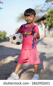 A Boy Playing Soccer In Front Of A House In Thailand Today.