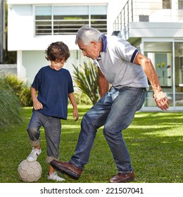 Boy Playing Soccer With His Grandfather In Garden In Front Of A House