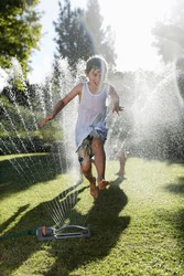 Boy Playing In Sprinkler In Backyard