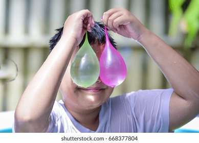 Boy playing water balloons in pool and look at this by his eyes in many color water balloons.