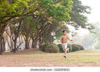 Boy playing with windmill, running, jumping in the park on summer vacation concept for freedom or the environment