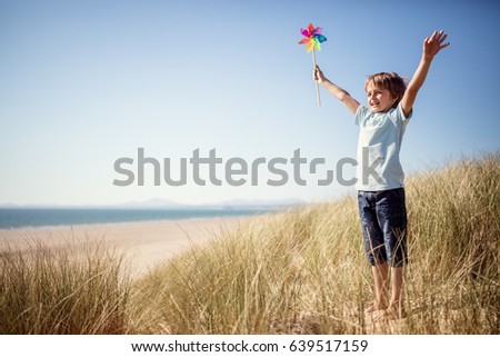 Boy playing with windmill in sand dunes at the beach on summer vacation concept for freedom or the environment