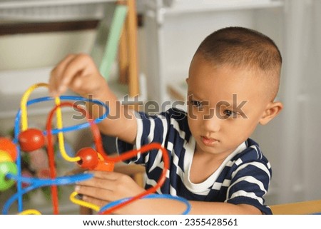 boy plays with developmental toys on the table inside the house. By sliding the ball along the curved steel