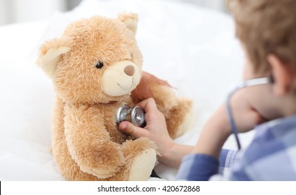 Boy plays in doctor with stethoscope and Teddy Bear.