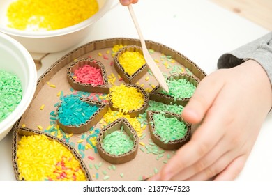 Boy Plays With Green Color Rice. Implement For Children To Develop Fine Motoric Skills Through Play. DIY Toy To Learn Hand - Eye Coordination.