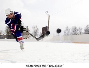The boy plays hockey on a street skating rink.A boy on the street playing hockey.