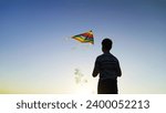 Boy plays kite with toy. Flying kite in blue sky, silhouette of child. Childhood, dream of flying, freedom travel. Happy boy playing with multi colored flying kite in nature in rays of summer sun.