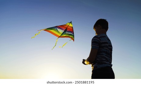 Boy plays kite with toy. Flying kite in blue sky, silhouette of child. Childhood, dream of flying, freedom travel. Happy boy playing with multi colored flying kite in nature in rays of summer sun. - Powered by Shutterstock