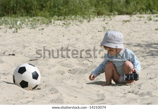 The boy plays on sand with the toy automobile\
near to a football