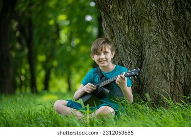 a boy plays a small guitar, a black ukulele on a bench in the park	 - Shutterstock ID 2312053685