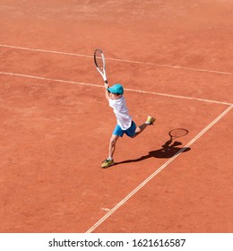 A boy plays tennis on a clay court. A little tennis player focused on the game and shot in flight after hitting the ball. Tennis kid. Sports action frame. Active games. Square size.