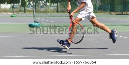 A boy plays tennis on the tennis court. Half body of a young tennis player and shadow on the court. Athlete in action. Children's tournament match. Active sport. Copy space.