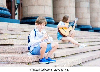 A Boy Plays A Wind Instrument On The Steps Of A Music School Outside.