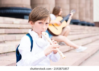 A Boy Plays A Wind Instrument On The Steps Of A Music School Outside.