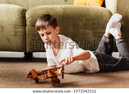 A boy plays with a wooden toy plane in the living room. Longing for travel