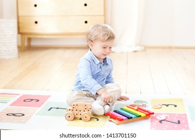 The boy plays xylophone at home. Cute smiling positive boy playing with a toy musical instrument xylophone in the children's white room. Close-up of kid playing on xylophone. Child development concept