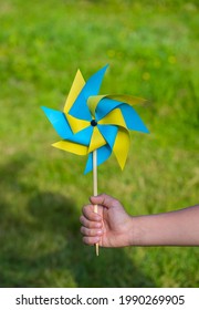 A boy plays with a yellow and blue paper 8-petal weather vane in the garden. Children's creativity, crafts.