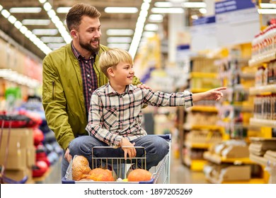 boy pointing finger at side in store, showing something to father, wants father to buy something in grocery market, sitting on cart