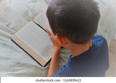 Boy praying with hands folded on a Bible