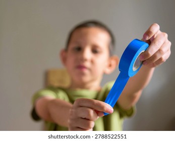 Boy pulling a strip of blue electrical insulation tape from a roll close up; conceptual for youthful curiosity in electronics, hands-on stem education workshop and home wiring safety skills