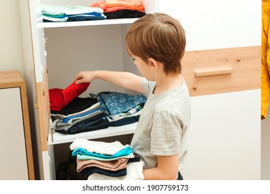 The Boy Puts Things In Order In The Closet. Kid Organizing Clothes In Wardrobe. Order In The Closet. Boy Putting Stack Of Clothes On The Shelf.