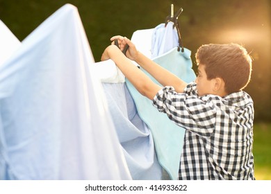 Boy Putting Bed Sheets Onto Homemade Tent In Garden