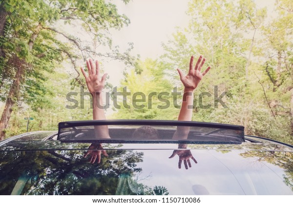 Boy putting his  hands out of the car\
sunroof top, driving down a country\
road