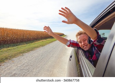 Boy putting his heads and hands out of the car window driving down a country road