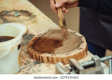 Boy is putting a protective mordant on the wooden disk, closeup. Young carpenter working with wood in craft workshop. Boy makes wooden clock in the workshop. - Powered by Shutterstock