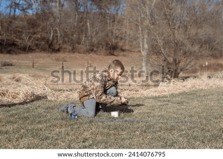 Boy putting work on fishing rod near pond