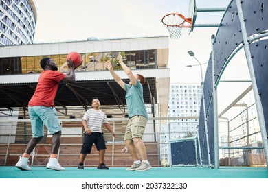 Boy Raising hands while making cuts under hoop while playing basketball with brothers on city playground