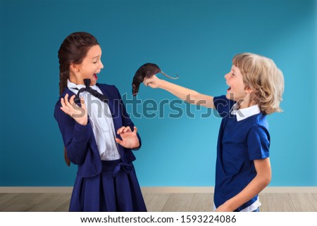 Boy with rat teasing scared girl at school. Psychological bullying concept,  tease, badger, taunt, mock, aggressive behavior. April Fool's Day joke