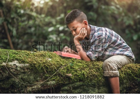 Boy reading book or holy bible on tree with moss. Children and religion.