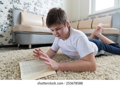 Boy reading a book while lying on a carpet in the room