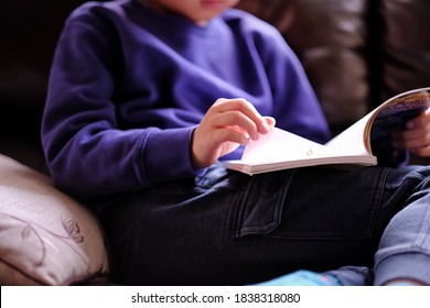 Boy reading children's book and flipping the page at home. Kid comfortable laying on sofa and enjoying the cartoon comics book during covid-19 pandemic lockdown. - Shutterstock ID 1838318080