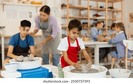 Boy in a red apron works at the potter's wheel and makes a product from clay. Child learns to sculpt from clay in a master class against the background of a teacher