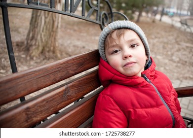 a boy in a red jacket and a gray hat in the city on a walk. Cool weather