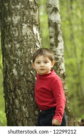 Boy in red jacket standing at tree at forest looking straight