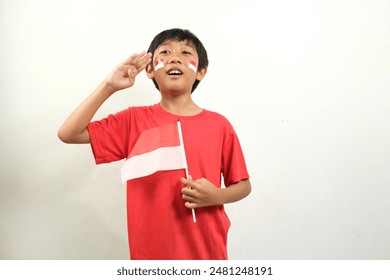 A boy in a red shirt proudly salutes while holding an Indonesian flag, showing patriotic enthusiasm. Ideal for content related to indonesia independence day celebrations, and patriotism. - Powered by Shutterstock