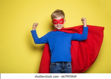 Boy in red super hero cape and mask. Studio portrait over yellow background - Powered by Shutterstock