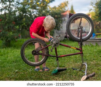 A Boy In A Red T-shirt Repairs A Bicycle. The Bike Is Upside Down On The Ground