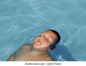 The Boy Relaxing In The Pool. Lying In The Water, He Closed His Eyes As The Sun Shines On His Face